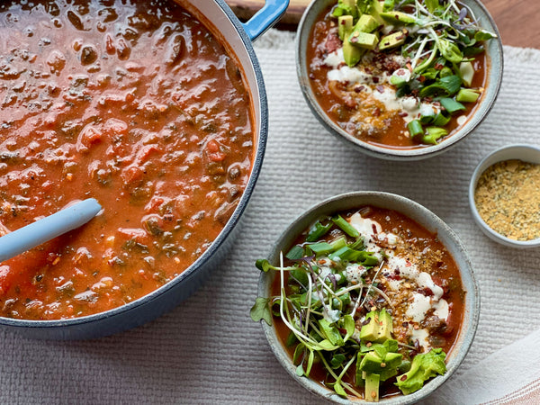 A pot of loaded tomato soup with two bowls filled with soup and topped with garnishes.