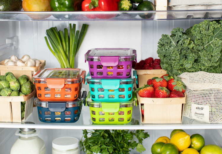 Colorful food storage containers on a refrigerator shelf with fresh produce.
