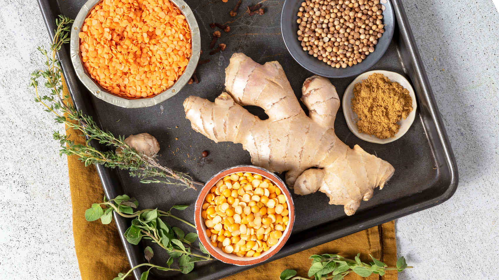 Spices and herbs on a baking tray with a focus on ginger and lentils.